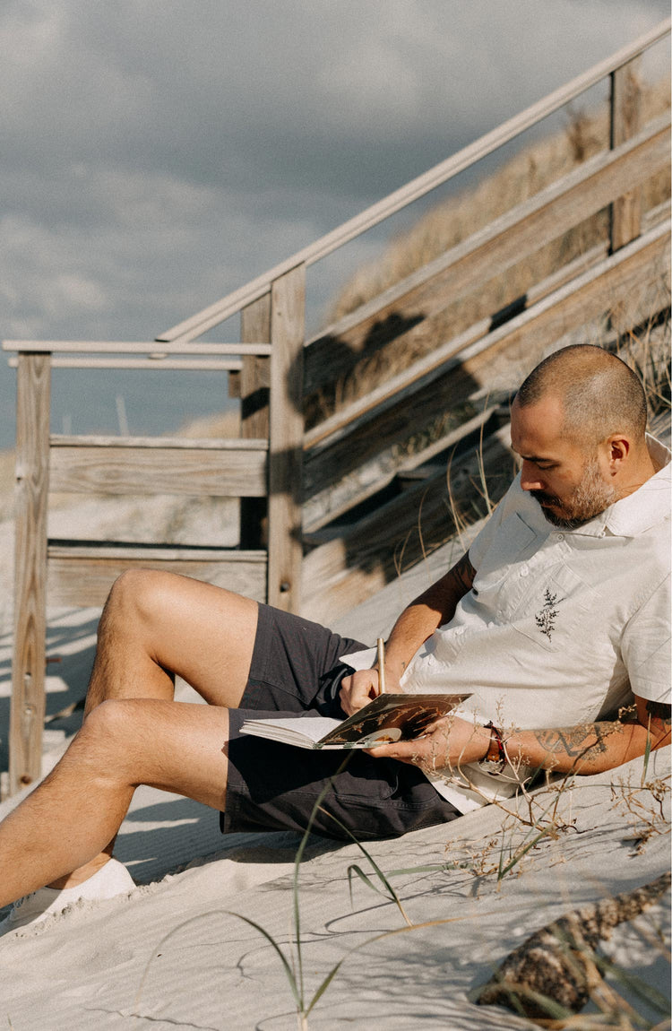 fit model sitting on the beach wearing The Apres Short in Organic Dark Blue Foundation Twill