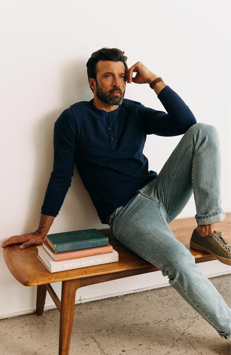 fit model sitting on a bench wearing The Heavy Bag Henley in Navy