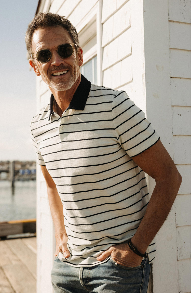 fit model leaning against the wall wearing The Organic Cotton Polo in Bleached Natural Stripe