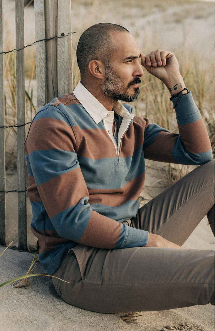 fit model sitting on the beach wearing The Rugby Shirt in Faded Brick Stripe