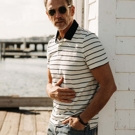 fit model leaning against the wall wearing The Organic Cotton Polo in Bleached Natural Stripe