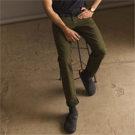 fit model sitting on a stool wearing The Slim Jean in Olive Nihon Menpu Selvage