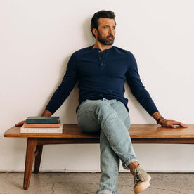 fit model sitting on a bench wearing The Heavy Bag Henley in Navy