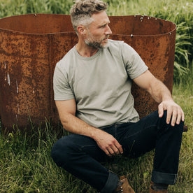 fit model sitting leaning against the wall in The Organic Cotton Tee in Sage